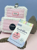 EverEmblem pre-cut cotton labels from the Strawberry Collection displayed with a pink and white crochet item, an iron, and label packaging. Perfect for personalizing handmade crafts