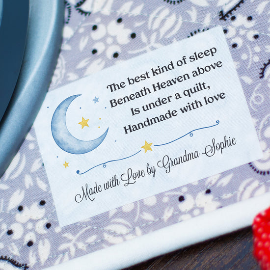 A close-up of a personalized quilt with a printed nursery poem on a white label, being ironed on a patterned fabric surface with a teal iron visible on the left and a red textured fabric on the right.